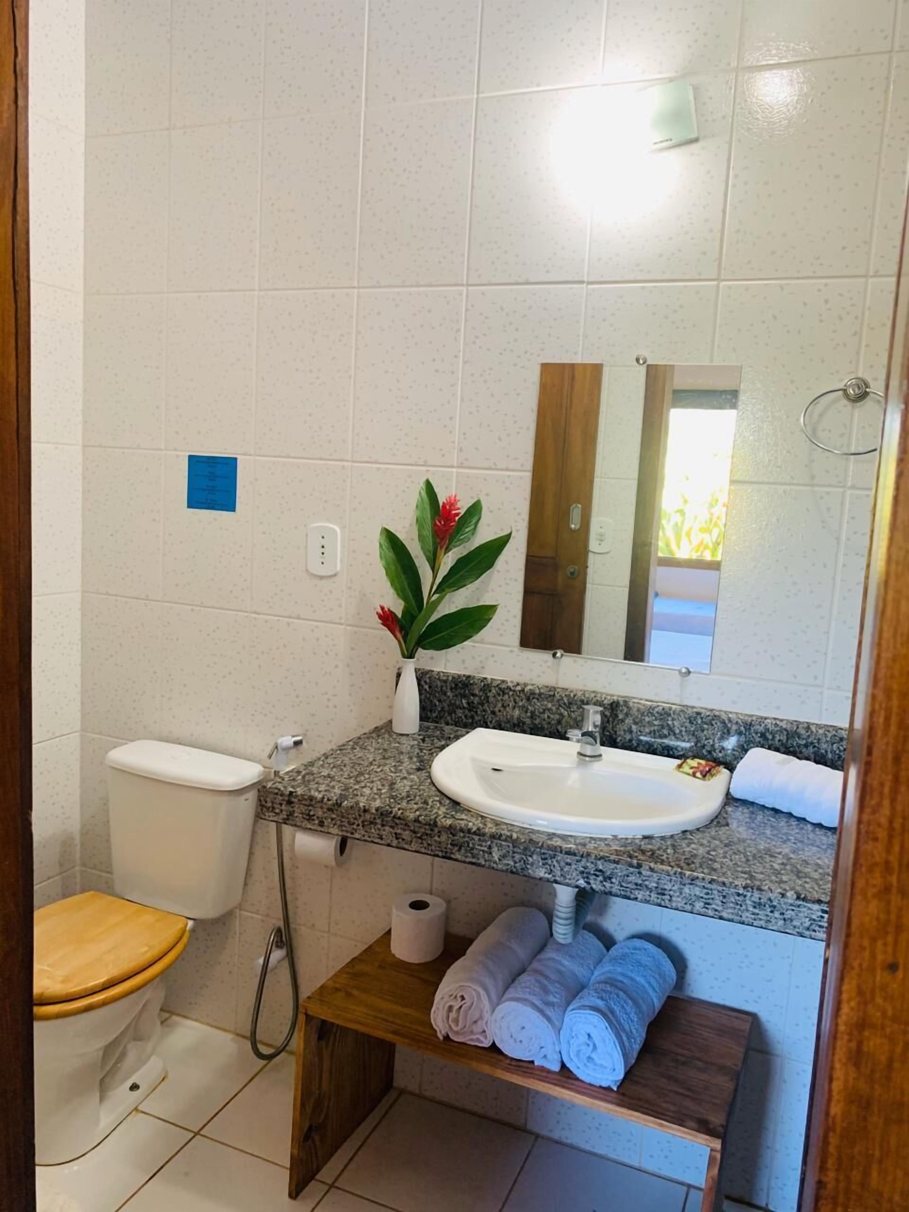 A bathroom with a toilet, sink, mirror, and a small shelf with towels.