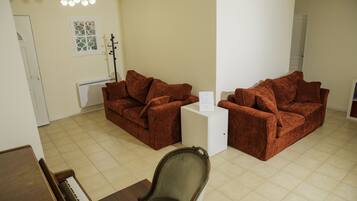 A living room with two brown sofas, a white side table, a wooden piano, and a decorative wall piece.