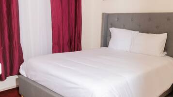 Una cama con cabecera gris, ropa de cama blanca y alfombra roja.
