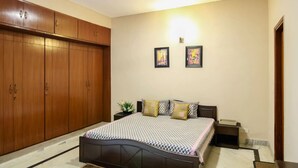 Un dormitorio con un armario amplio, una cama con ropa de cama estampada, dos cuadros en la pared y un ventilador de techo.