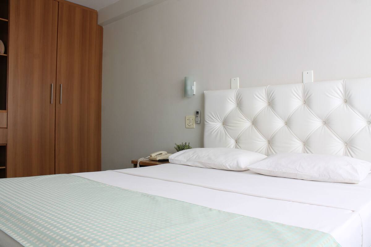 Een slaapkamer met een groot bed, een houten garderobe, een nachtkastje met een lamp en een wandlamp.