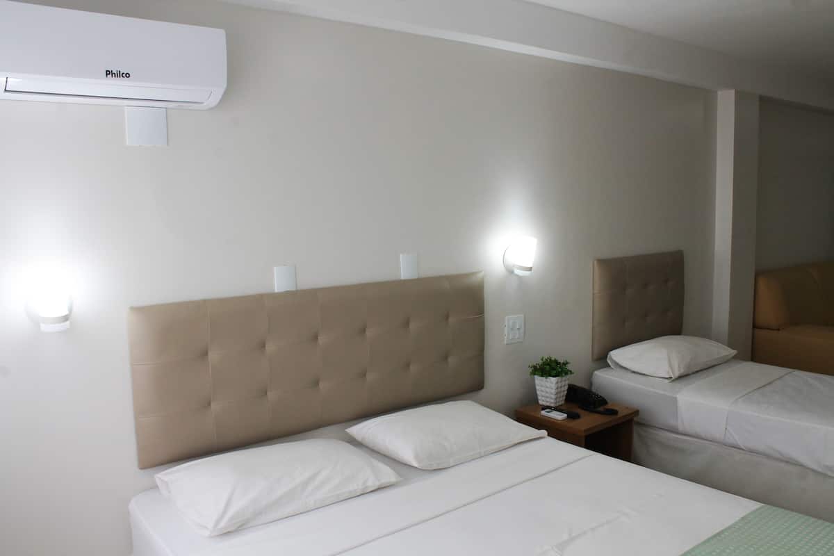 Een hotelkamer met twee bedden, een nachtkastje, een wandairconditioner en bedlampjes.
