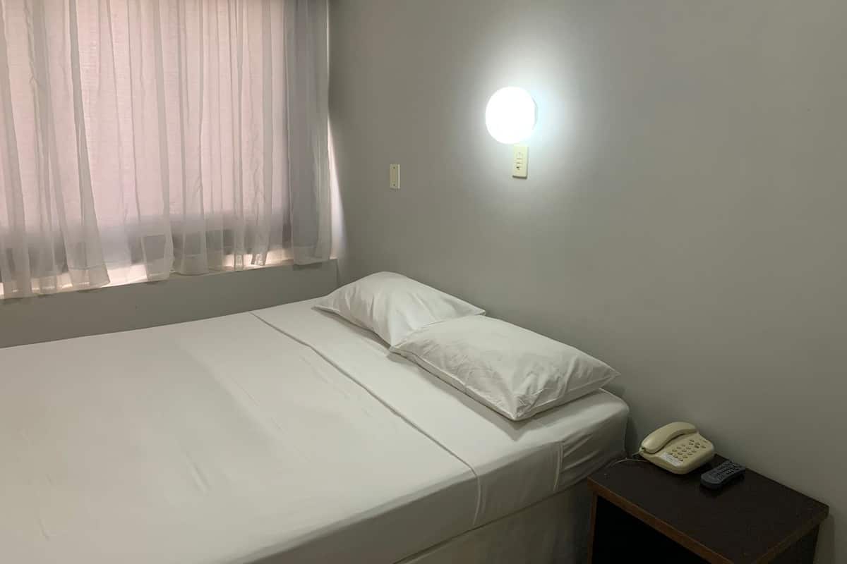 Een enkel bed met witte lakens, een bedtelefoon en een wandlamp.
