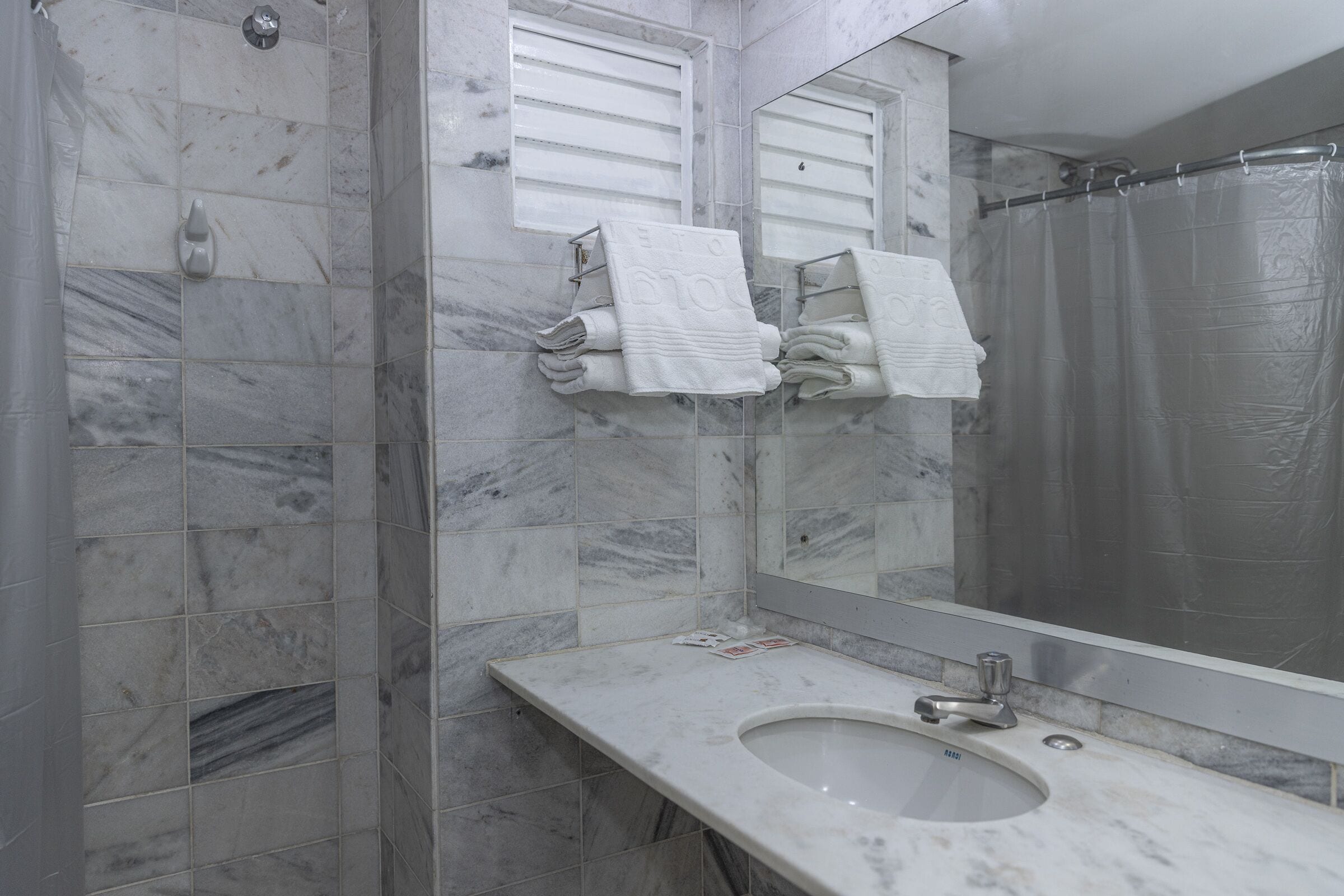 Un bany amb rajoles de marbre, un lavabo, un mirall i un tendal de banyera.