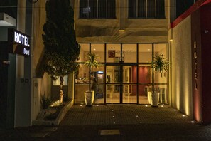 A hotel entrance with a sign reading "HOTEL Doral," large potted plants, and a paved walkway leading to the entrance.