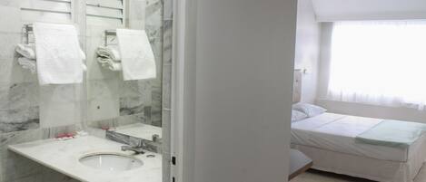 A bathroom with a marble sink, a mirror, and a bed with a green blanket in the adjacent room.