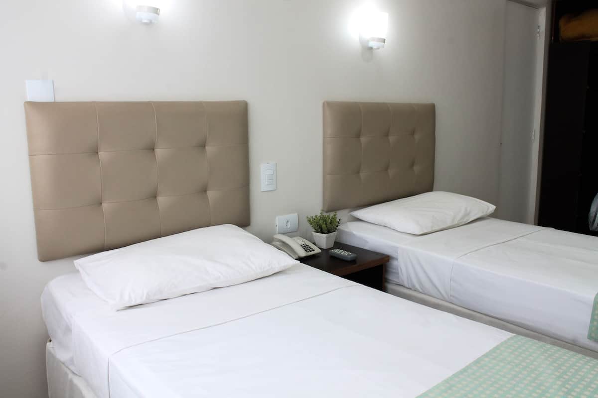 Een hotelkamer met twee bedden, elk met hoofdeinde en witte beddengoed. Er staat een nachtkastje met een lamp, telefoon en een klein plantje.