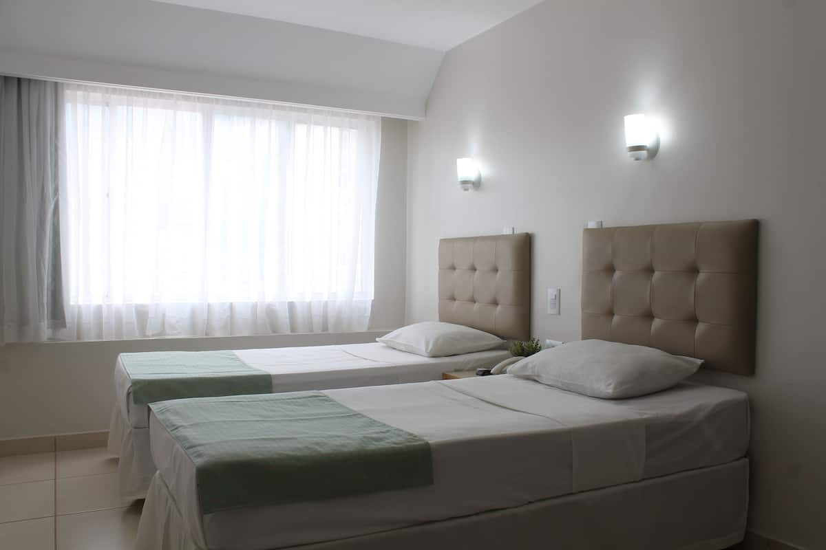 Een hotelkamer met twee bedden, een groot raam met dunne gordijnen en een wandlamp.