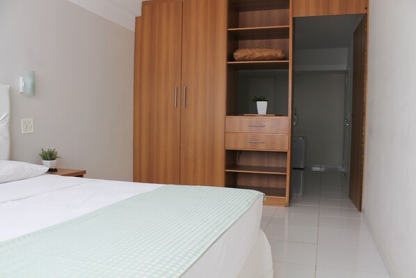 A bedroom with a bed, a wardrobe, a nightstand, and a small potted plant.