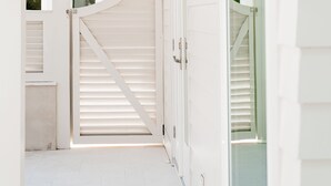 A white interior hallway with a wooden staircase, a door with a white shutter, and a small hanging light fixture. - Elegant Cottage on the Bluff Downtown Fairhope (A) (Fairhope)