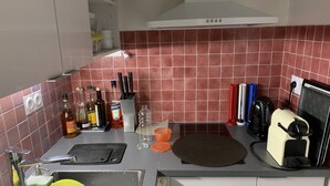A kitchen with a sink, countertop, and various kitchen items like bottles and utensils. - Appart central near Louvre  (Paris)