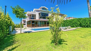 Une maison moderne dotée d’une piscine, d’un patio couvert et d’une pelouse bien entretenue.