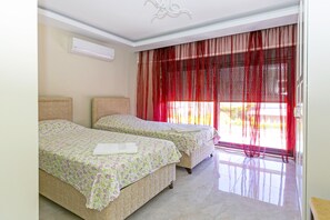Habitación de hotel con dos camas, un ventanal con cortinas rojas y aire acondicionado en el techo.