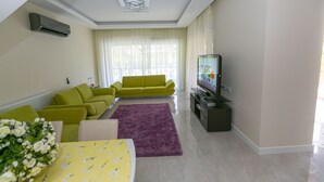Un salon avec un canapé vert, un téléviseur à écran plat et un tapis violet.
