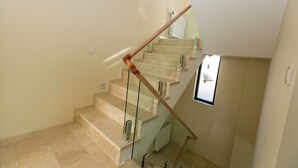 Un escalier avec des rampes en bois et des garde-corps en verre, menant à un palier doté d’une petite fenêtre.