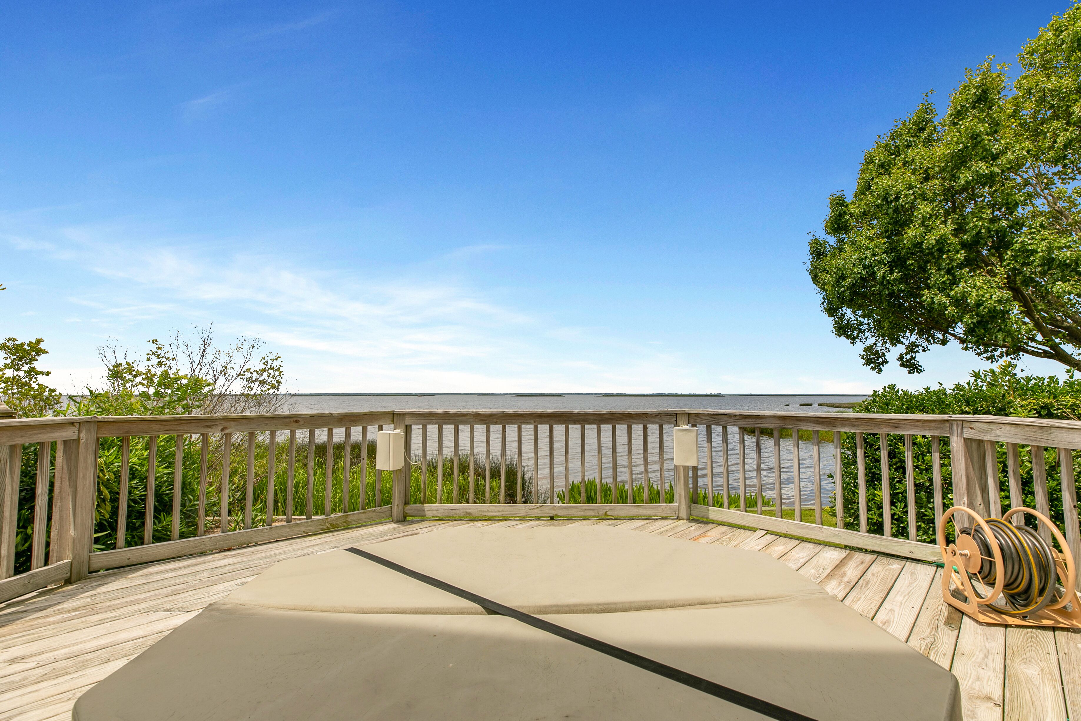 A wooden deck with a concrete seating area overlooking a body of water, surrounded by greenery.