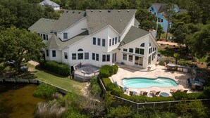 A large house with a swimming pool, a deck, and a view of the surrounding forest. - Sound Escape: Elevator, Hot Tub, Private Pool, Soundfront Location (Corolla)