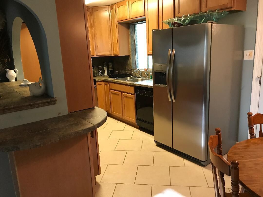 A kitchen with wooden cabinets, a stainless steel refrigerator, a sink, and a dining area with a wooden table and chairs.