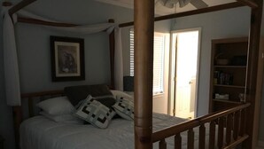 Ein Schlafzimmer mit einem Himmelbett, einem Nachttisch, einem Bücherregal und einem gerahmten Bild an der Wand.