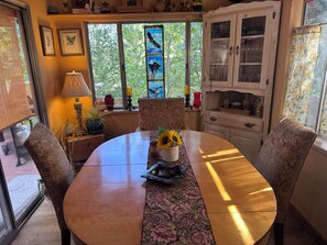 Ein Essbereich mit einem runden Tisch, Stühlen, einer Tischdecke mit Blumenmuster und einer Vase mit Sonnenblumen.