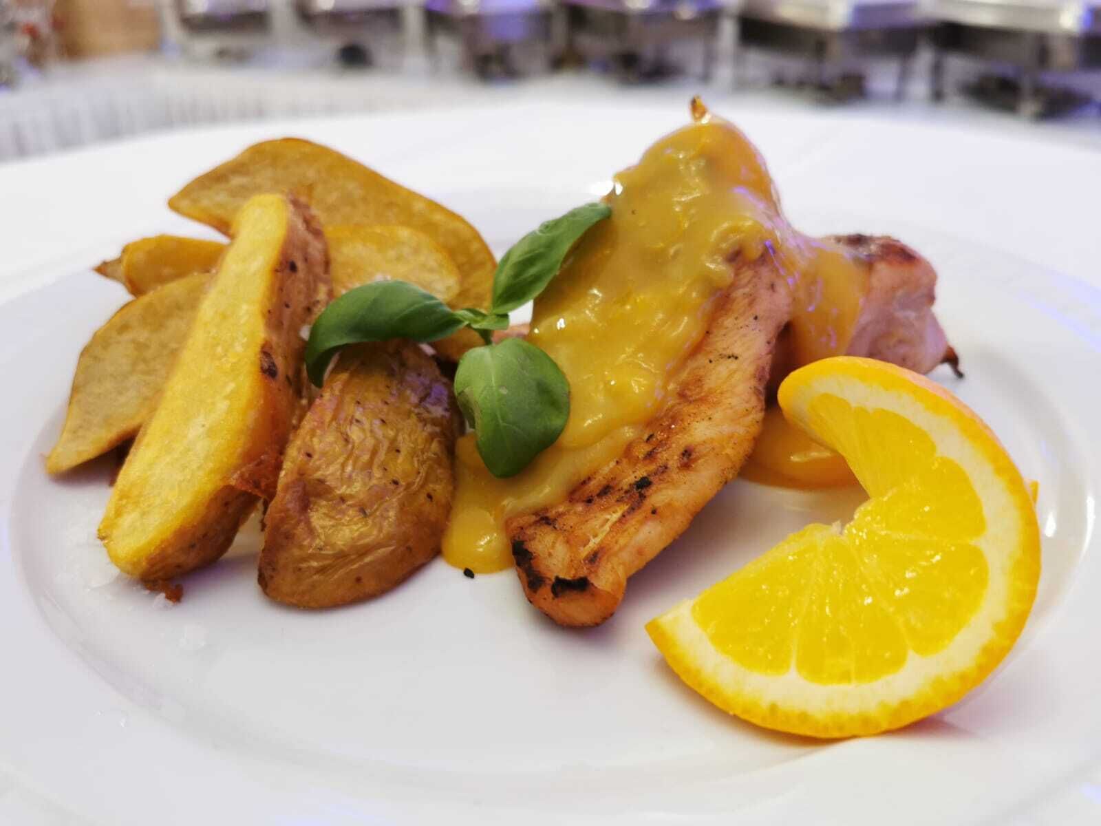 A plate with grilled chicken, potato wedges, and a slice of orange.