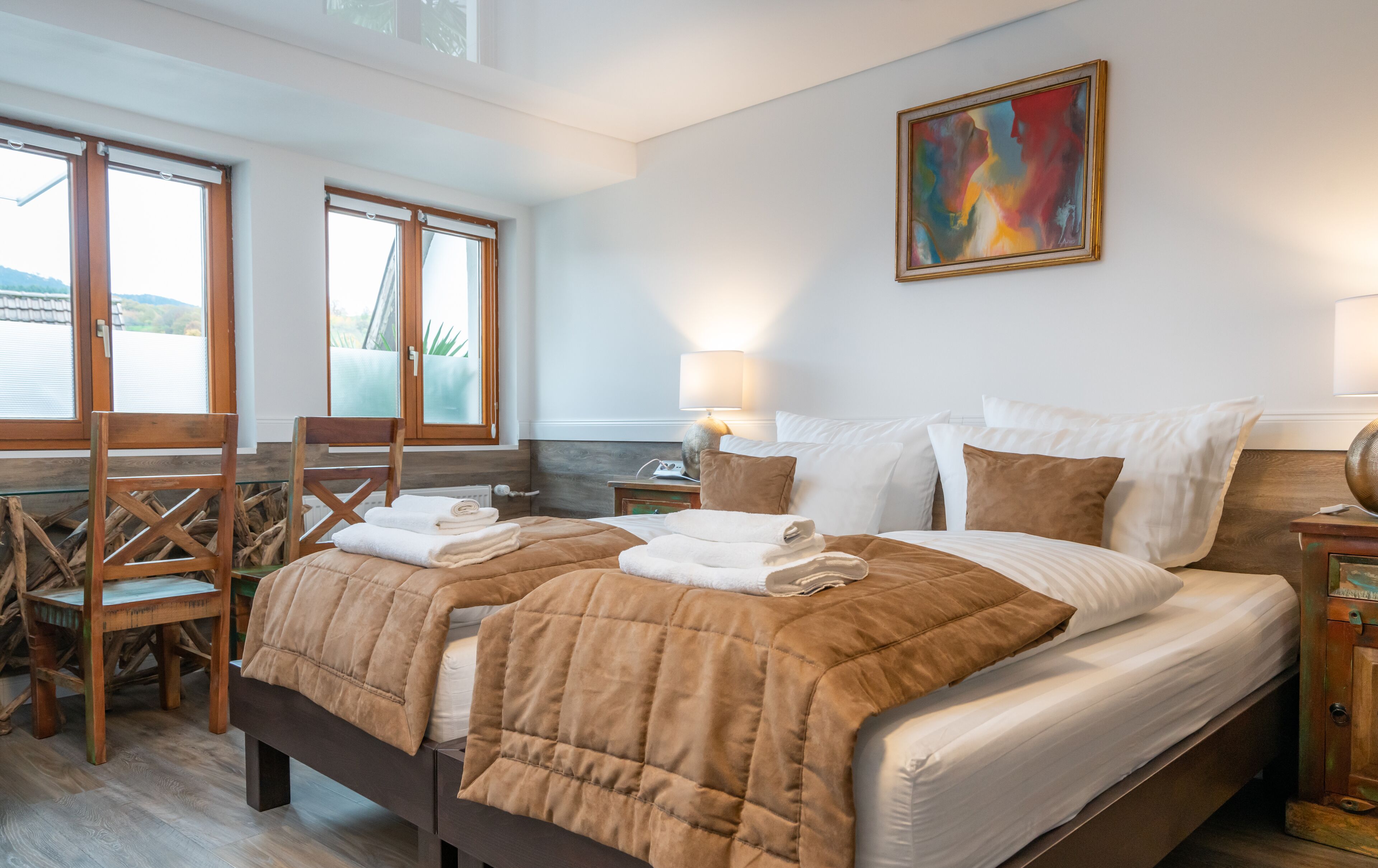 A well-lit bedroom with a large bed, a chair, a table, and a painting on the wall.