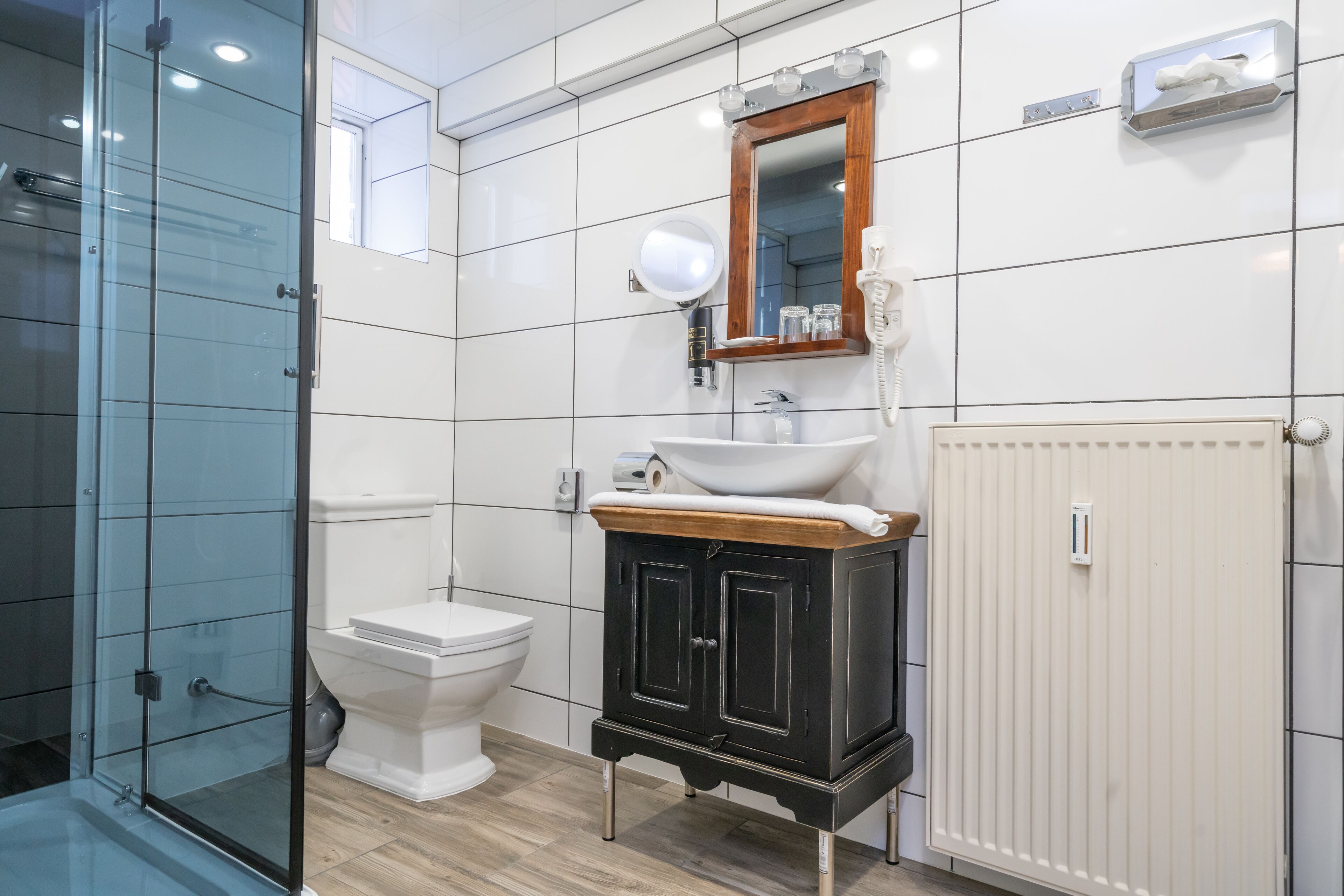 Un baño moderno con cabina de ducha de vidrio, inodoro blanco, tocador con encimera de madera y espejo sobre el lavabo.