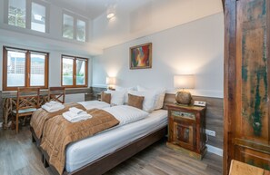 A bedroom with a large bed, two bedside tables, a wooden bench, and a view of the outdoors through large windows. - Landgasthaus Kreuz Michelbach (Gaggenau)