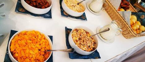 Un bufé de desayuno con tazones de cereal, leche y frutas.