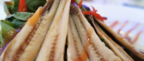 Un primo piano di un piatto con pesce a fette, guarnito con peperoni rossi e foglie verdi.