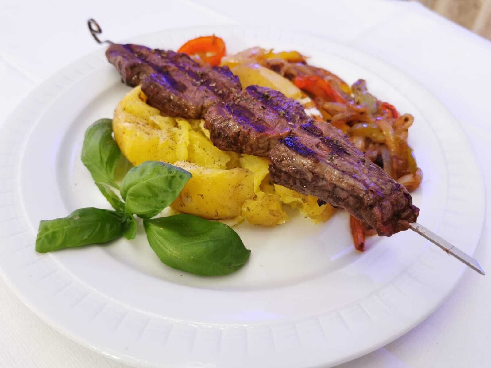 A plate with grilled meat skewers, mashed potatoes, and a garnish of basil leaves.