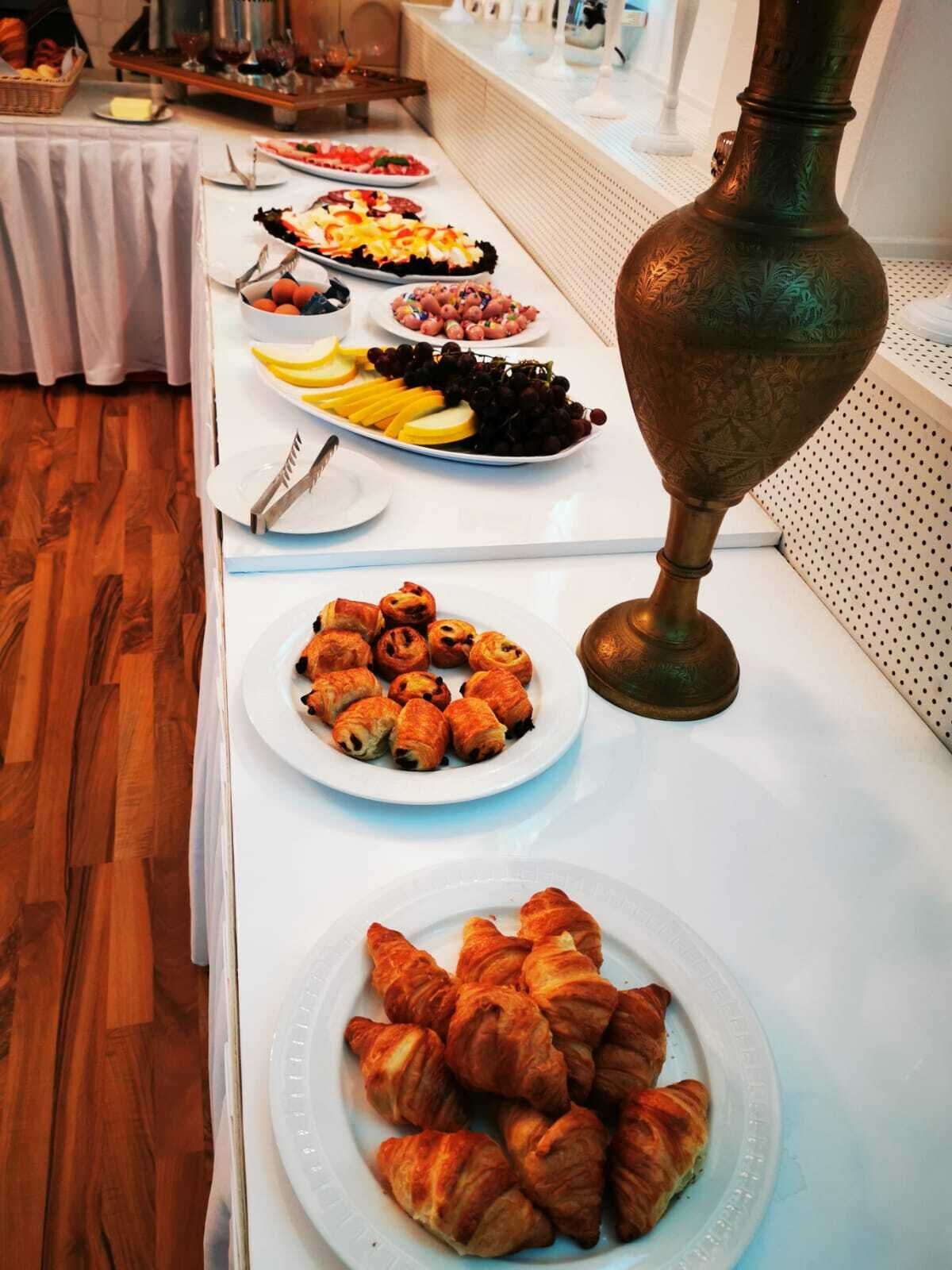 Une table de buffet proposant divers plats, notamment des pâtisseries, des fruits, et agrémentée d’un vase décoratif en laiton.