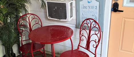 A red metal table and chairs outside a building with a window, a door, and a sign with a message.