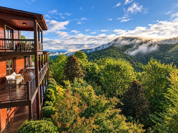 A multi-level wooden cabin with outdoor seating and a scenic mountain view.