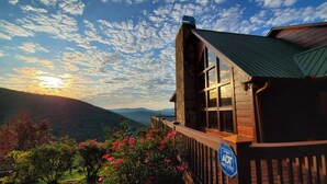 Une cabane en bois dotée d’un balcon donnant sur un paysage montagneux au coucher du soleil.