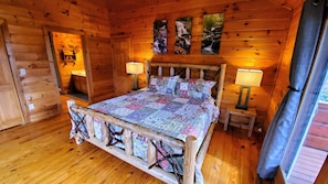 Dormitorio de cabaña de madera con cama, dos lámparas de noche y una ventana con cortinas.