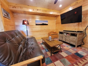 Interior acogedor de una cabaña con un sofá de cuero, una mesa de centro de madera, un televisor y un pequeño armario de madera.