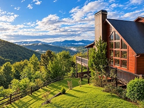A wooden cabin with large windows, surrounded by a well-maintained lawn and a wooden fence.