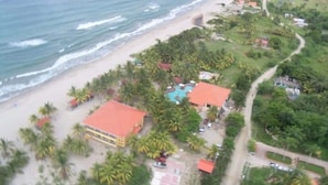 Vista aérea de un complejo turístico frente al mar, con playa, palmeras y piscina.