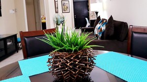 A dining area with a table set for two, featuring a unique centerpiece of sticks and green plants.