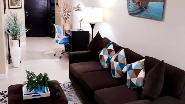 A living room with a brown sofa, patterned rug, and a painting of a boat on the wall.
