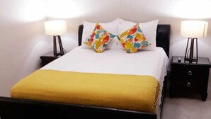 A neatly made bed with a yellow throw, two matching pillows, and two bedside lamps on black nightstands.
