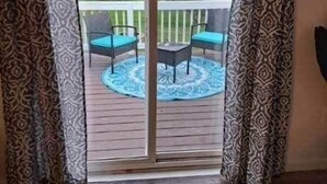A room with a sliding glass door leading to an outdoor deck with two chairs and a table.