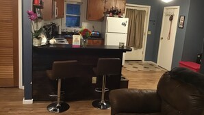 A kitchen with wooden cabinets, a refrigerator, and a bar area with stools.