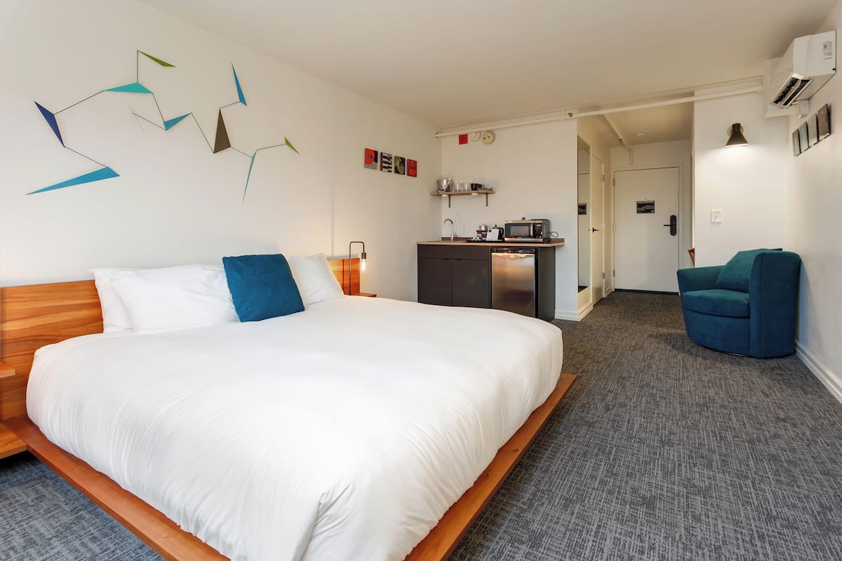 Quarto de hotel moderno com uma cama grande, uma mesa com micro-ondas e uma cadeira.
