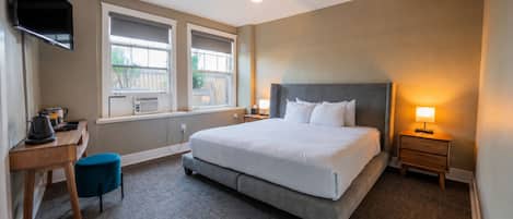A hotel room with a large bed, a desk with a chair, a television mounted on the wall, and a window with an air conditioning unit.