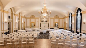 A large banquet hall with rows of white chairs, round tables, and a grand chandelier. - Hotel Leo (Bellingham)