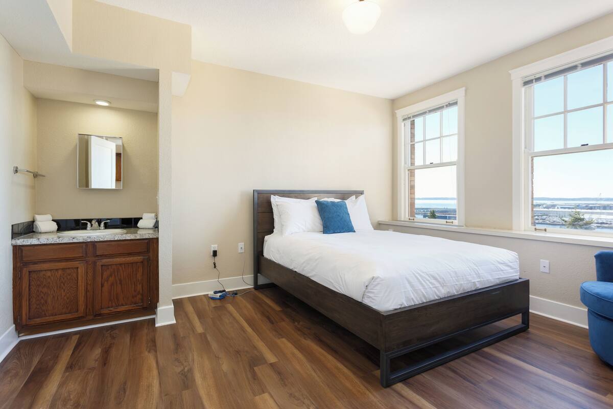 Quarto com cama de madeira, banheiro com toucador e janelas amplas com vista.