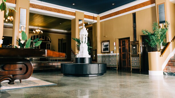 A lobby with a central fountain, a reception desk, and a staircase. - Hotel Leo (Bellingham)