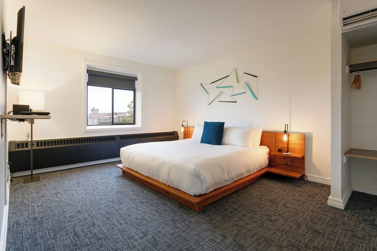 Quarto de hotel moderno com uma cama grande, janela, radiador e televisão montada na parede.